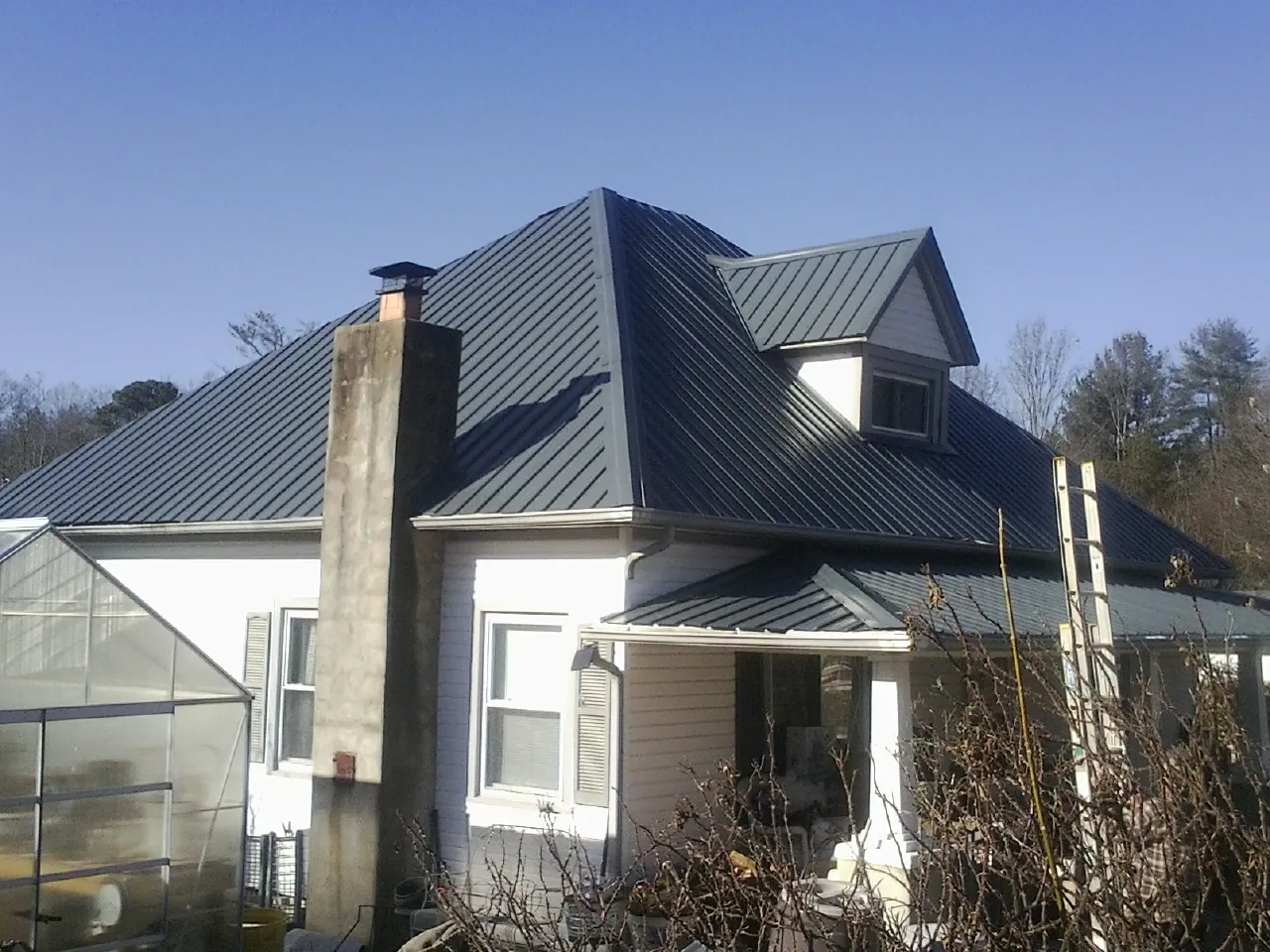 Dark blue standing seam metal roof on a white farmhouse with dormer — Slate & Tile Roof Repair by Roofing Brothers in Saint Henry