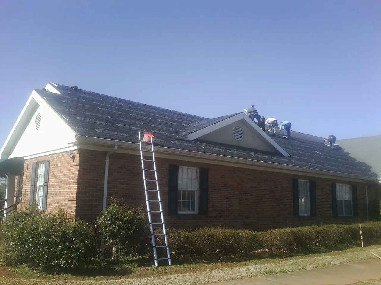 Crew tearing shingles off a brick ranch roof with a ladder set — Emergency Roof Repair work by our crew in Saint Henry
