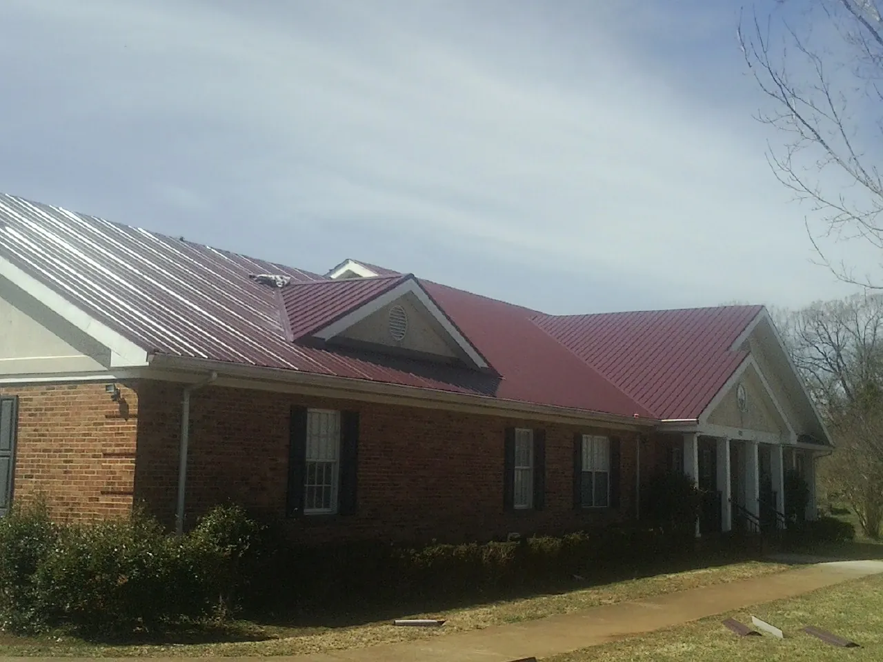 Red metal roof with gabled entries on a long brick building, from a Hail Damage Roof Repair job in Saint Henry