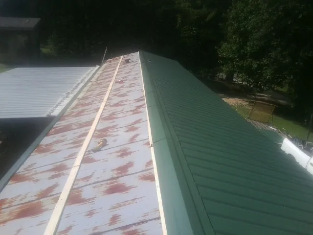 Old rusted panels beside newly installed green metal roofing — Wind Damage Roof Repair by Roofing Brothers in Saint Henry