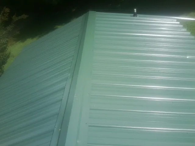 New green metal panels meeting at the ridge of a roof — Flat Roof Repair work by our crew in Saint Henry