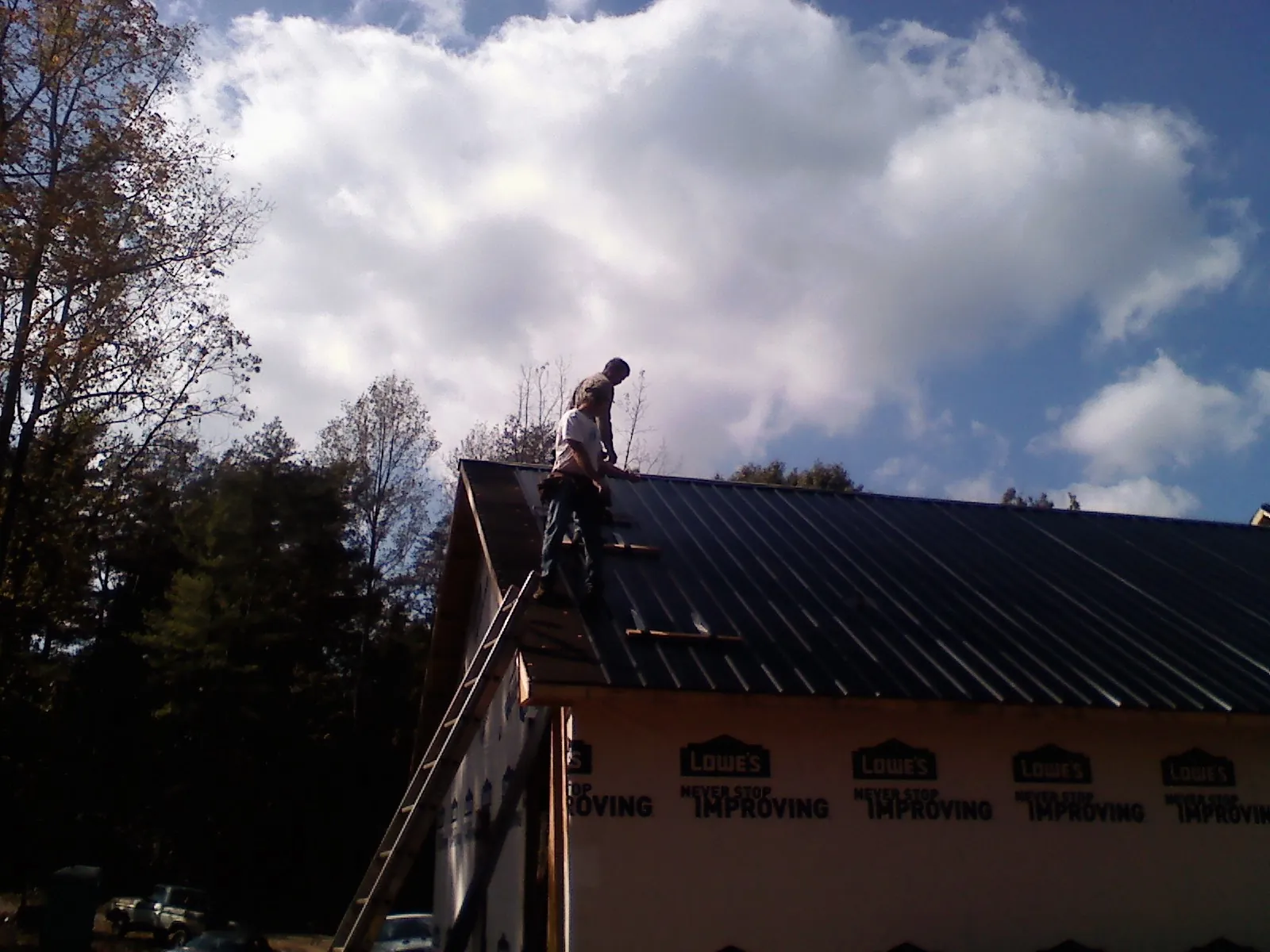 Roofer fastening dark metal panels high against a cloudy sky, from a Roof Inspection job in Saint Henry