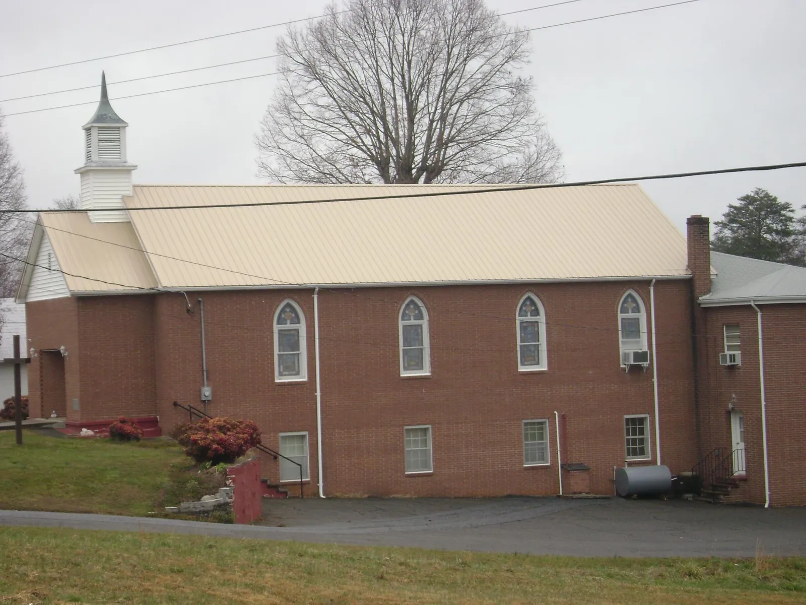 New tan metal roof on a brick church with a white steeple in Saint Henry