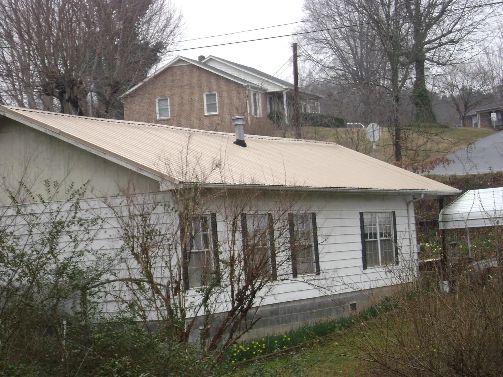 Tan metal roof on a white sided house set into a hillside — Commercial Roofing by Roofing Brothers in Saint Henry