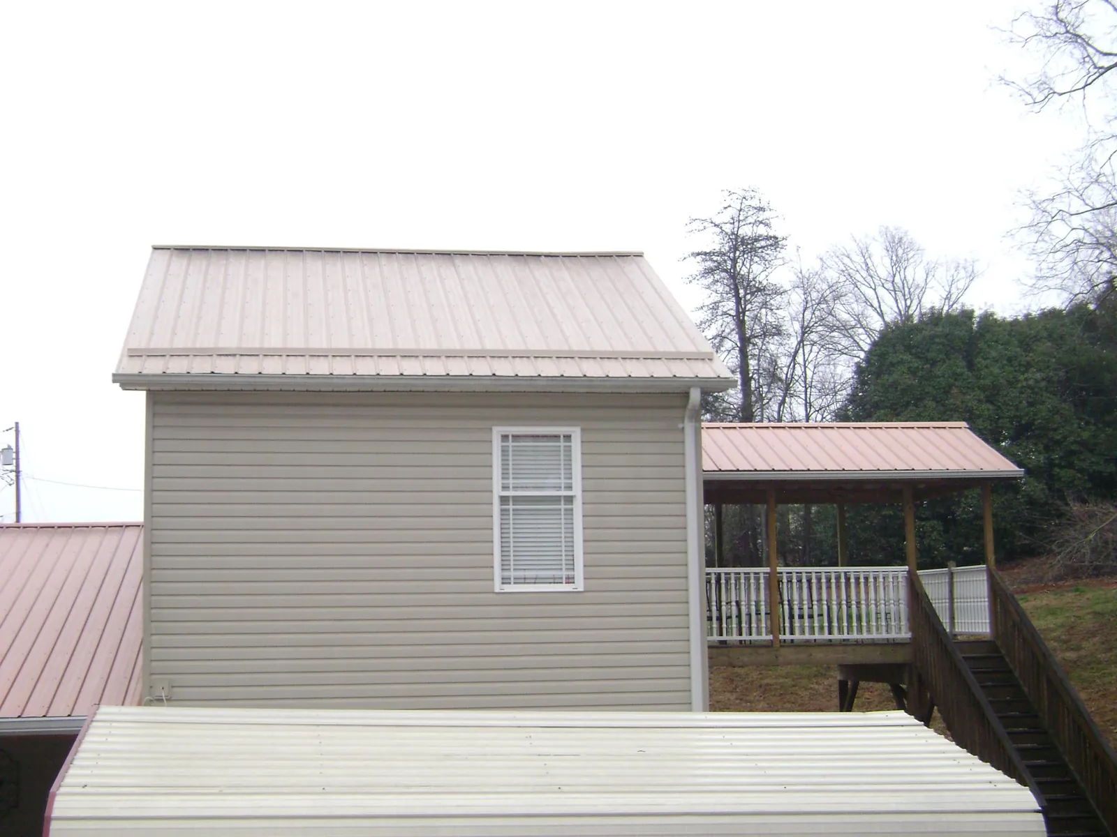 Tan metal roofs on a two story addition and attached porch, from a Roof Replacement job in Saint Henry